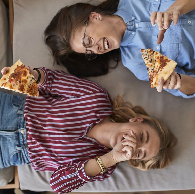 two-laughing-young-women-lying-down-eating-pizza-royalty-free-image-916900176-1563391386
